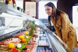 Happy,Young,Woman,Choosing,Meat,From,Glass,Cabinet,In,Grocery