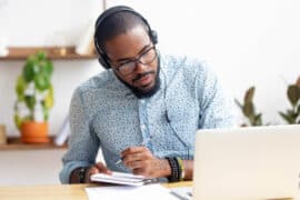 Focused,African,Business,Man,In,Headphones,Writing,Notes,In,Notebook