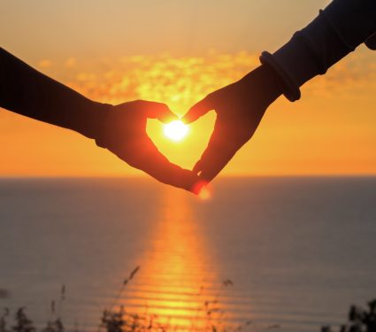 two hands of lovers on the background of sunset on the sea