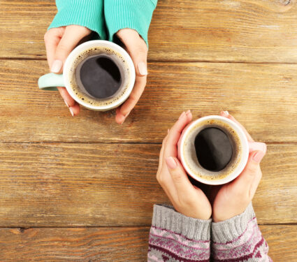 Female,Hands,Holding,Cups,Of,Coffee,On,Rustic,Wooden,Table