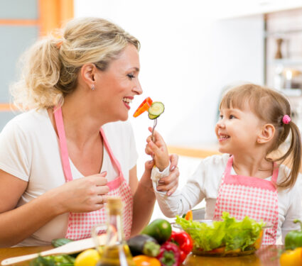 Kid,Daughter,Feeding,Mother,Vegetables,In,Kitchen