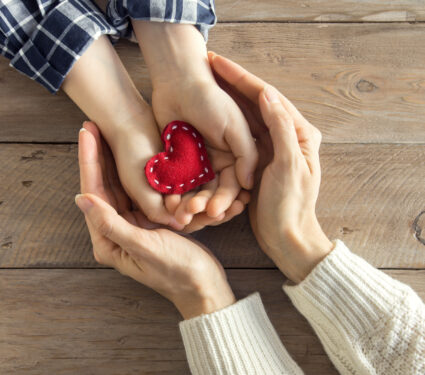Red,Heart,In,Child,And,Female,Hands,Over,Wooden,Background,