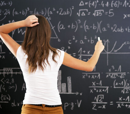 Young,Woman,Looking,At,Math,Problem,On,Blackboard